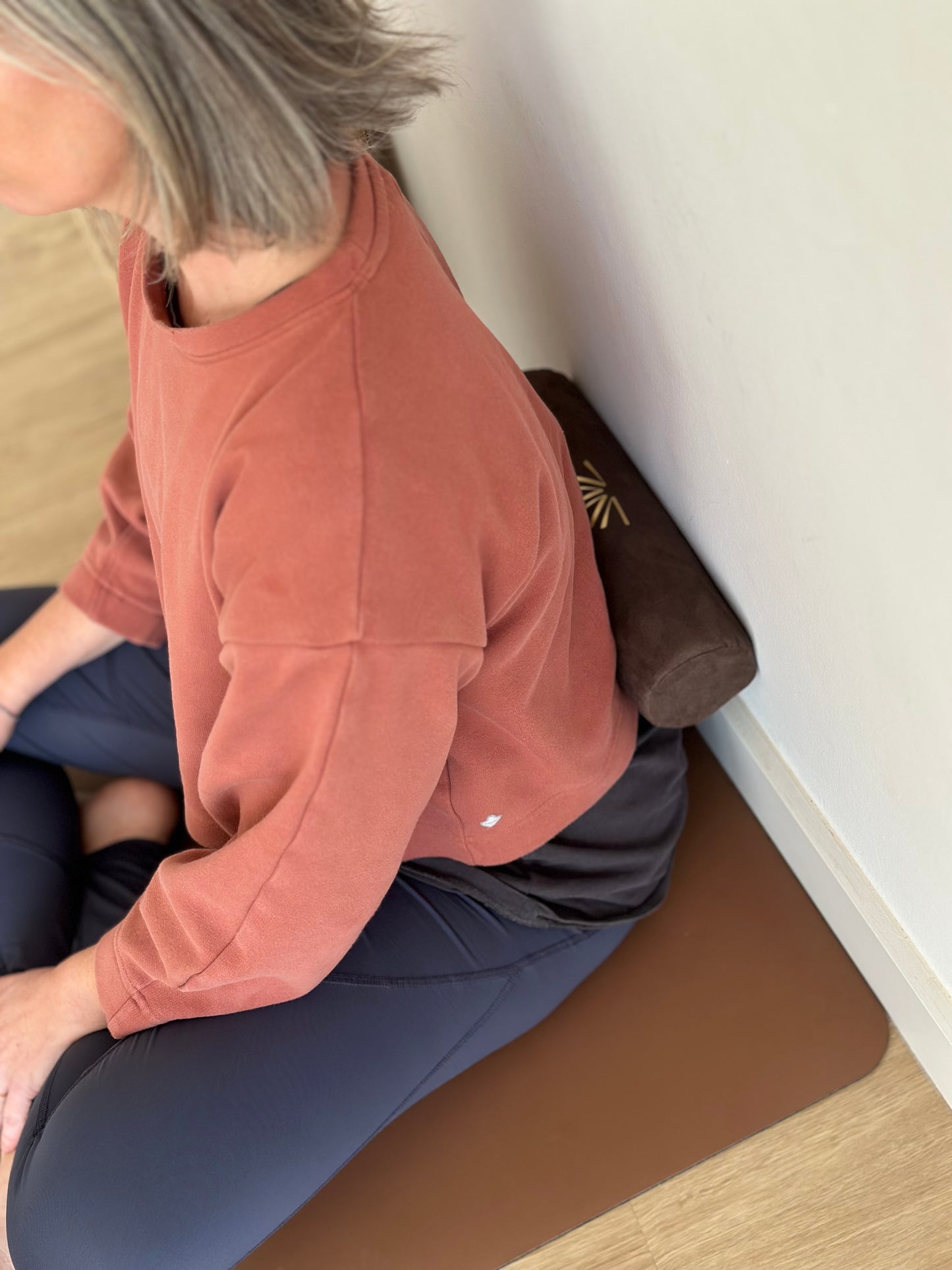 Person sitting on a yoga mat with an Axis Roll in the lumbar area, leaning against a wall.