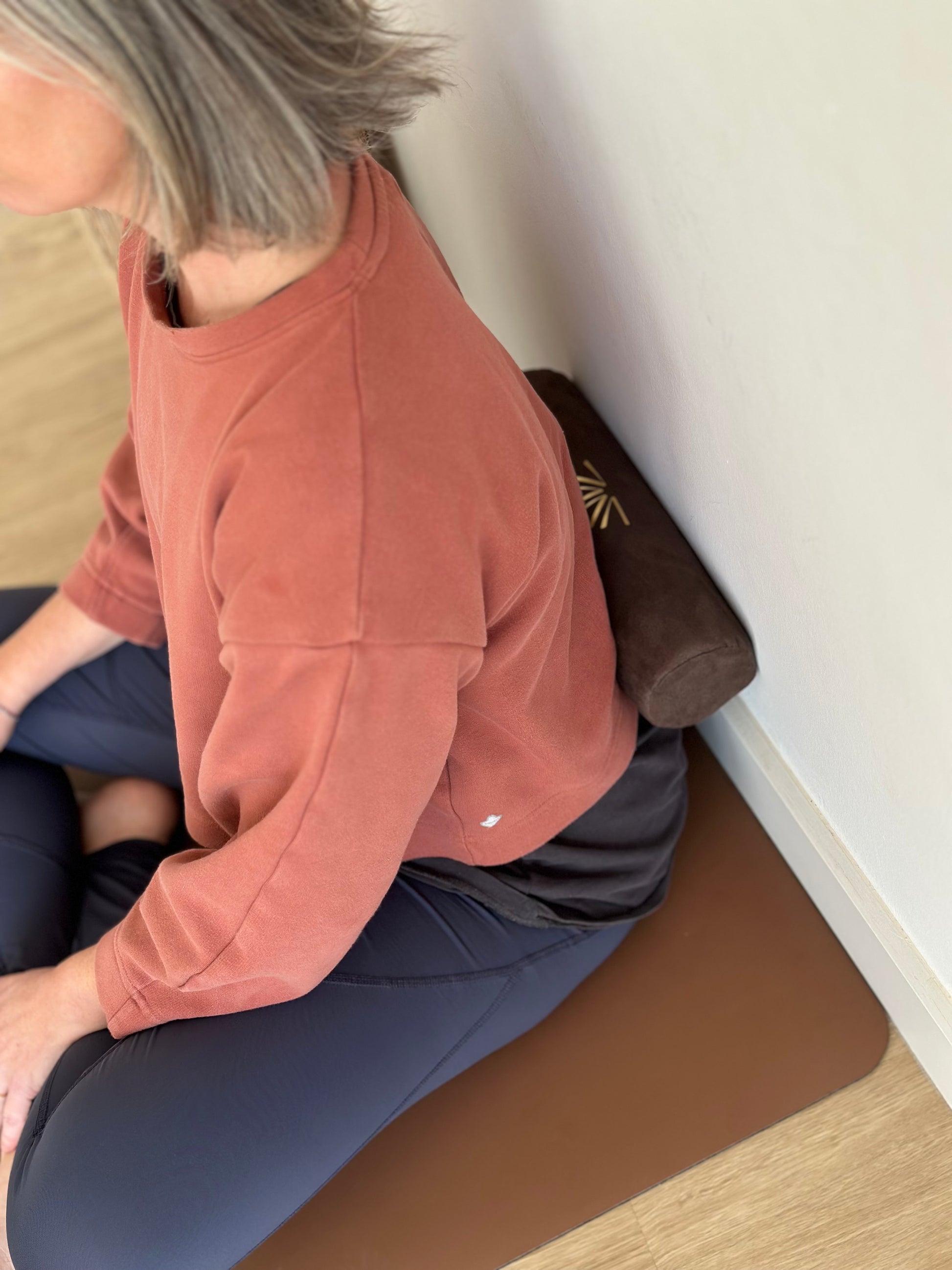 Person sitting on a yoga mat with an Axis Roll in the lumbar area, leaning against a wall.
